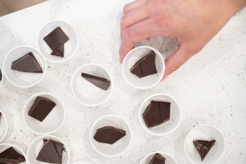 Hand reaching for sample sized pieces of dark chocolate placed in white paper cups