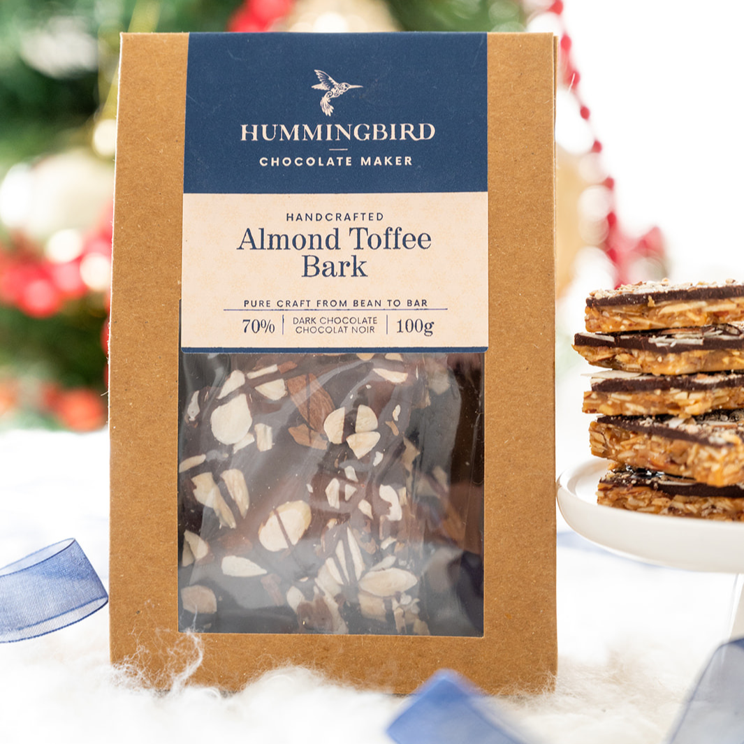 Almond Toffee Bark in beautiful craft box along with thick chocolate toffee bark outside packaging and in front of a festive background