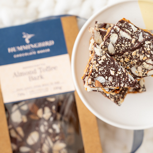 Close up of almond toffee chocolate bark, displayed on a white plate and with wrapped package in the background