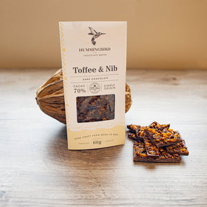 Hummingbird Chocolate Toffee & Nib bar leaning against a cacao pod and beside some chunks of the chocolate bar