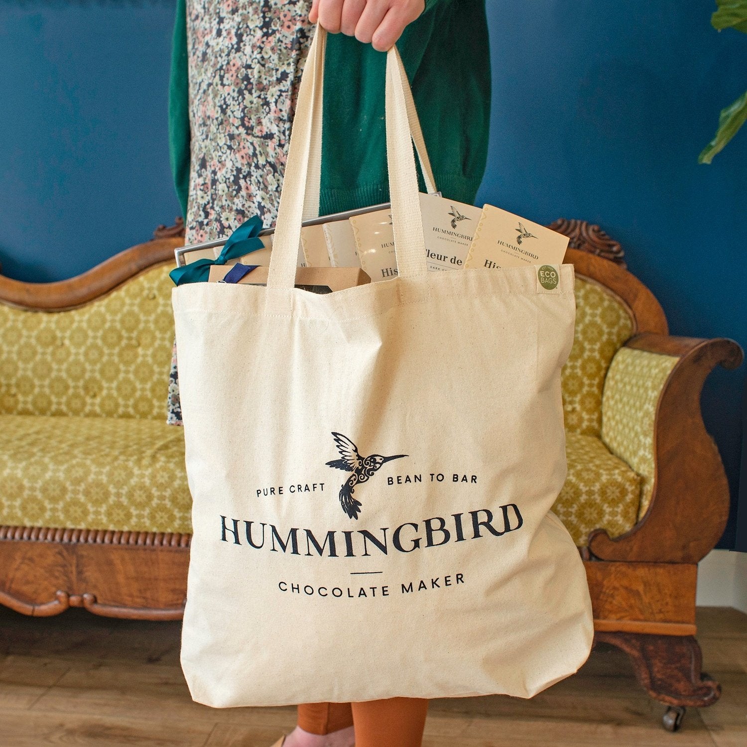 Hummingbird Chocolate Maker tote bag stuffed with bean-to-bar chocolate and being held by the handles