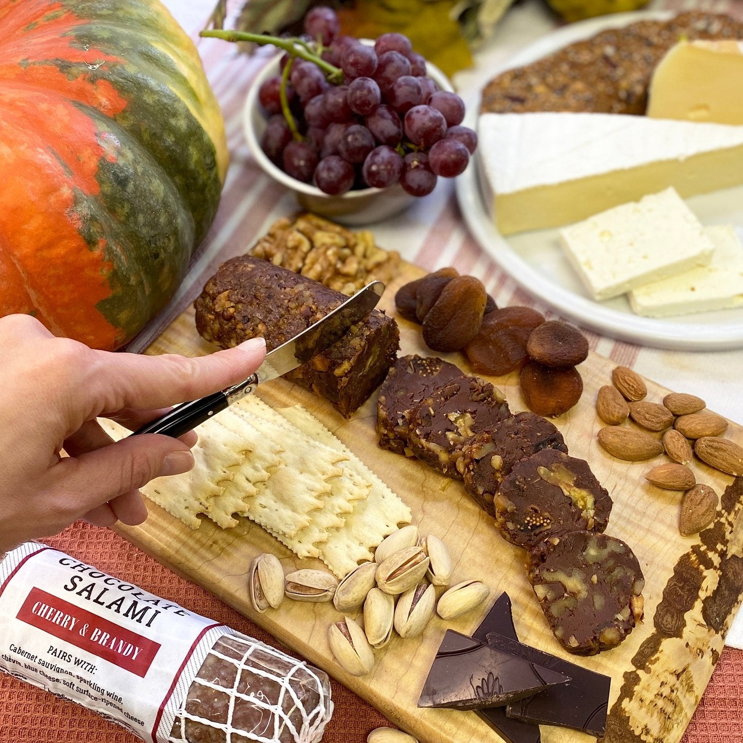 Cheese, fruit and sliced chocolate salami spread on a wood cutting board.