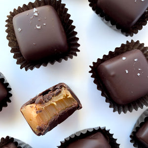 Close up of handcrafted chocolate covered caramels sprinkled with Canadian fleur de sel and one with a bite revealing the soft, chewy caramel center