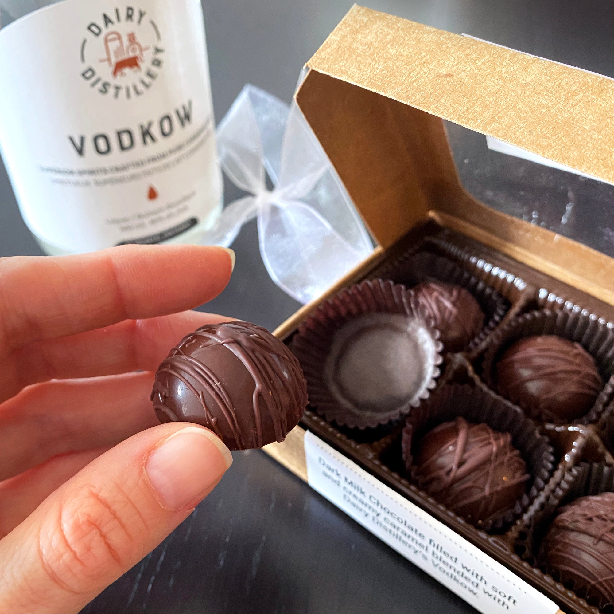 Hummingbird Chocolate, Box of 6 Vodkow Caramels, opened box showcasing the 6 pieces inside, with Dairy Distillery's Vodkow in the background.